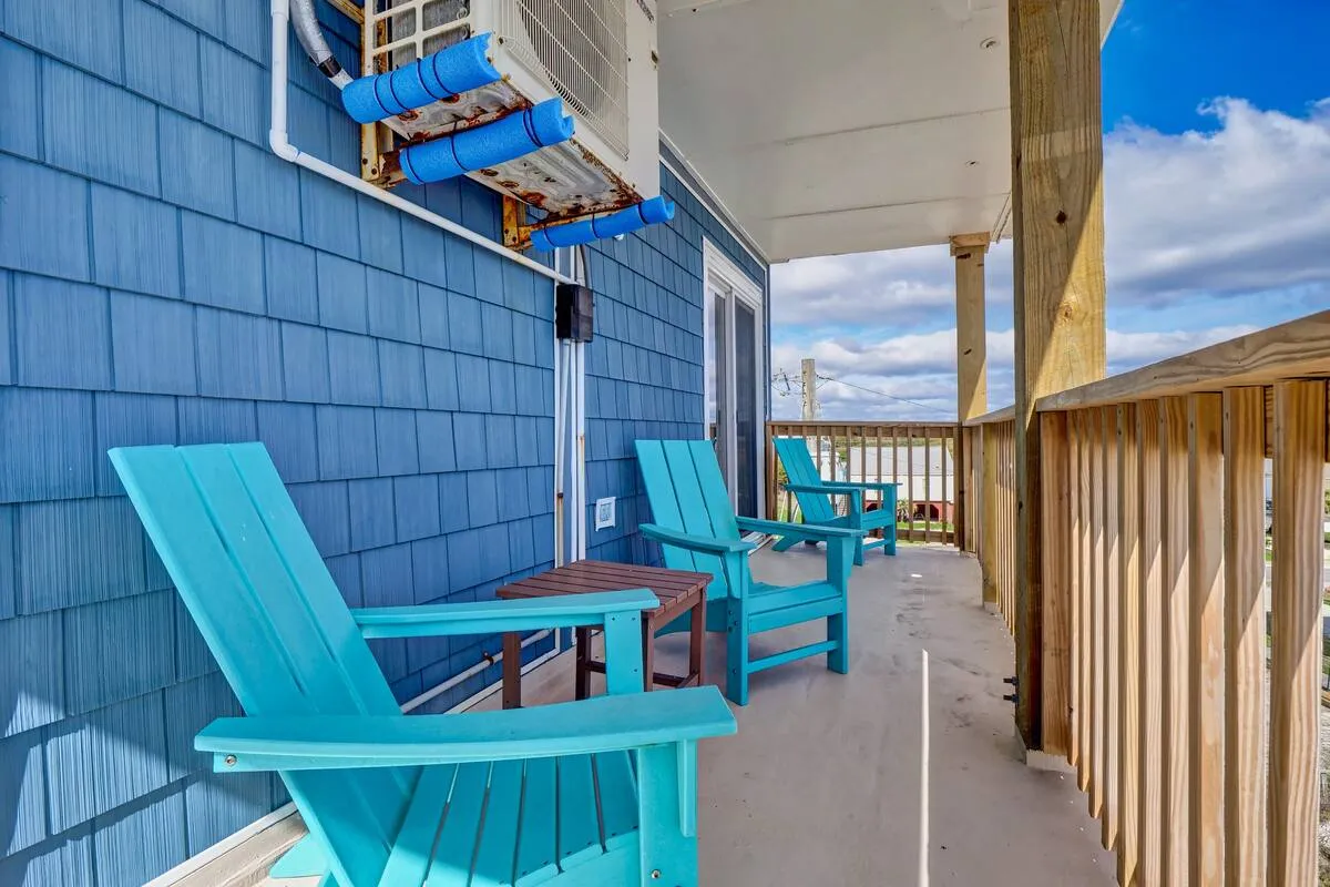 Tranquil exterior balcony with blue wooden chairs and a wooden railing, positioned to overlook the ocean. The scene evokes relaxation, with hints of enjoying morning coffee or quiet sunset reflection while immersed in coastal views.