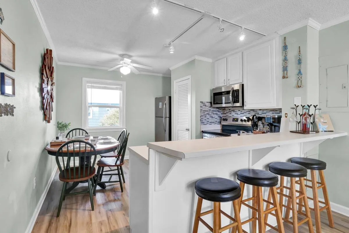 This image centers on a kitchen island and dining table, with decorative wall art and a prominent wall clock in view. The scene is warmly lit, suggesting a space where cooking, dining, and socializing seamlessly blend together.