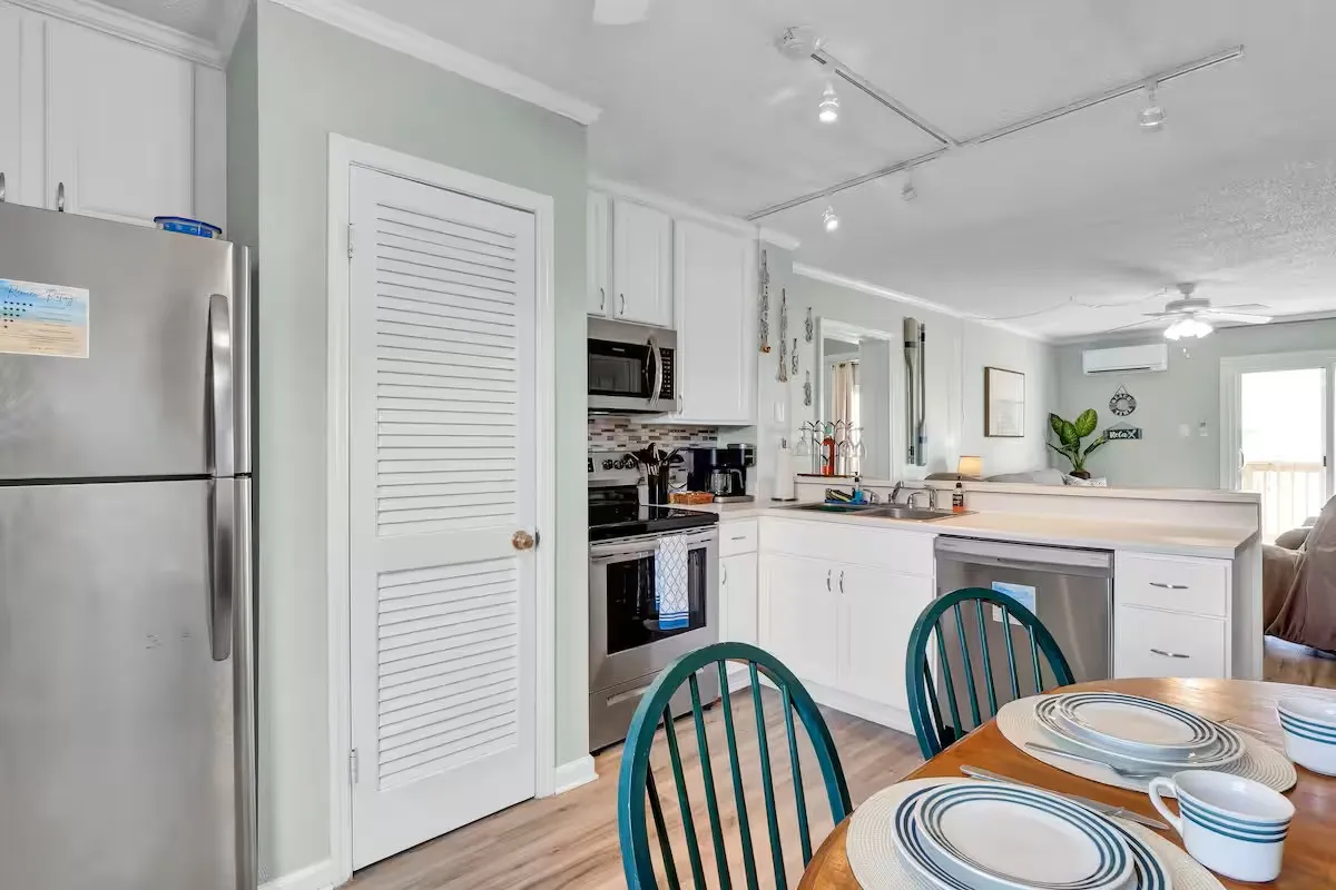 A cozy kitchen with a well-set countertop, green dining chairs, appliances, and a welcoming table arrangement. The image highlights both the preparation and dining aspects of the space.